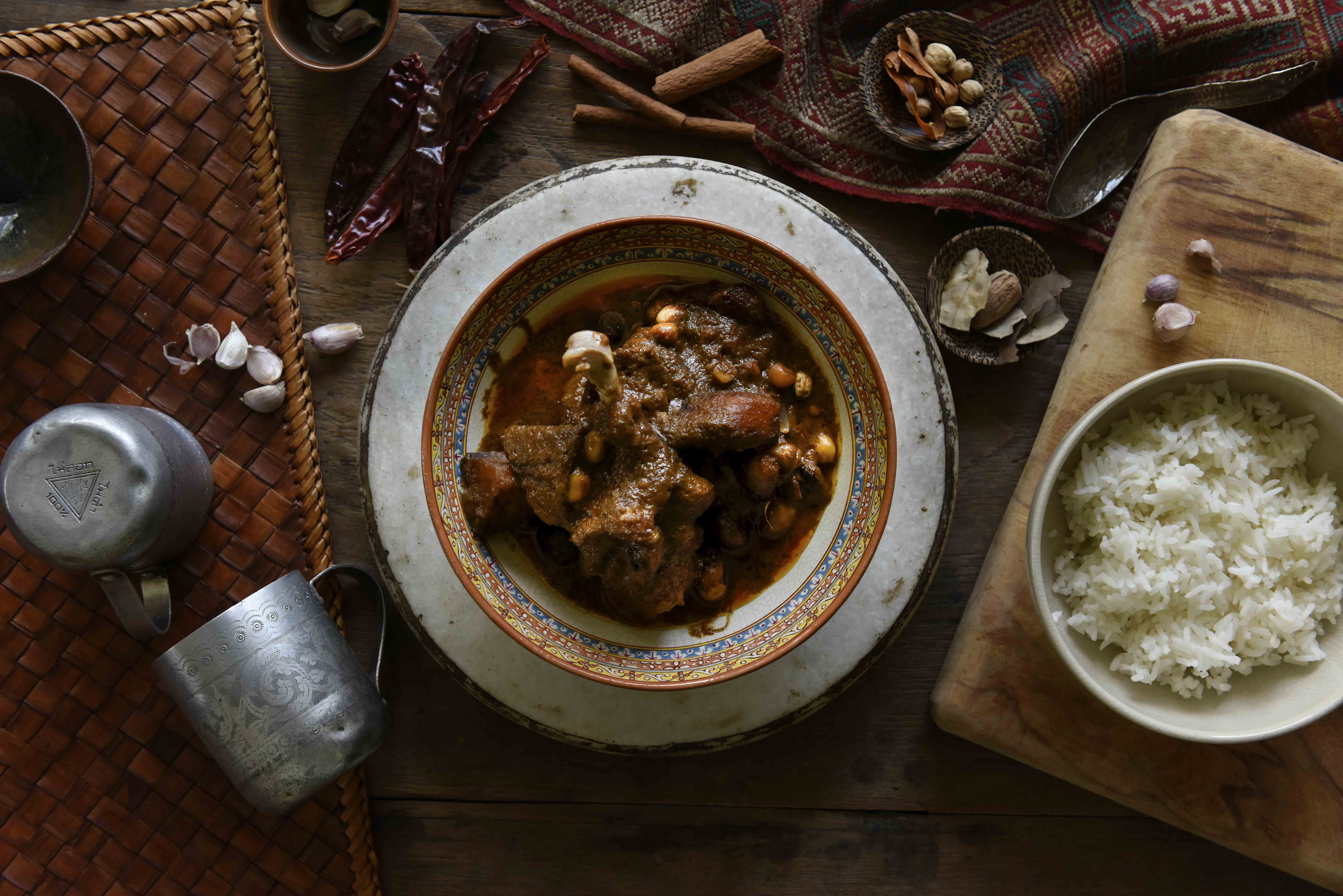 Editorial overhead — Thai curry in an ornate ceramic bowl with traditional props, styled cookbook composition