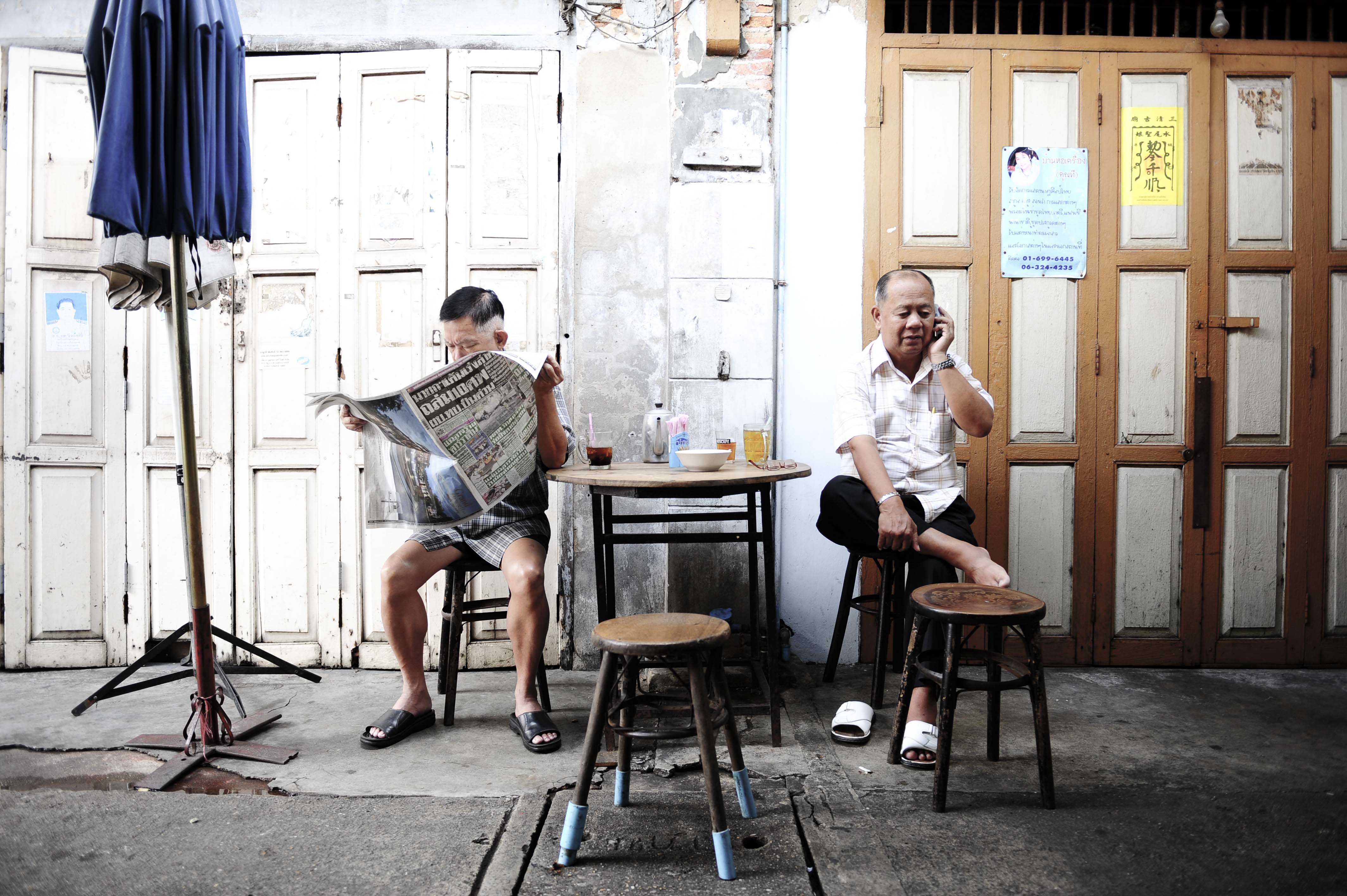 Editorial photograph — two men outside a Bangkok shophouse, morning light